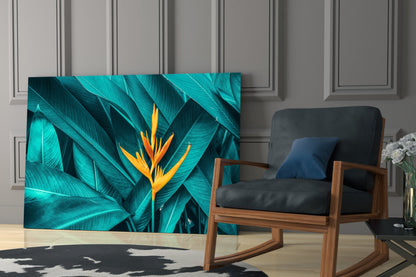 Tropical Leaf 3 glass wall art displaying turquoise banana leaves with yellow-orange bird of paradise flower, installed in modern living room interior.