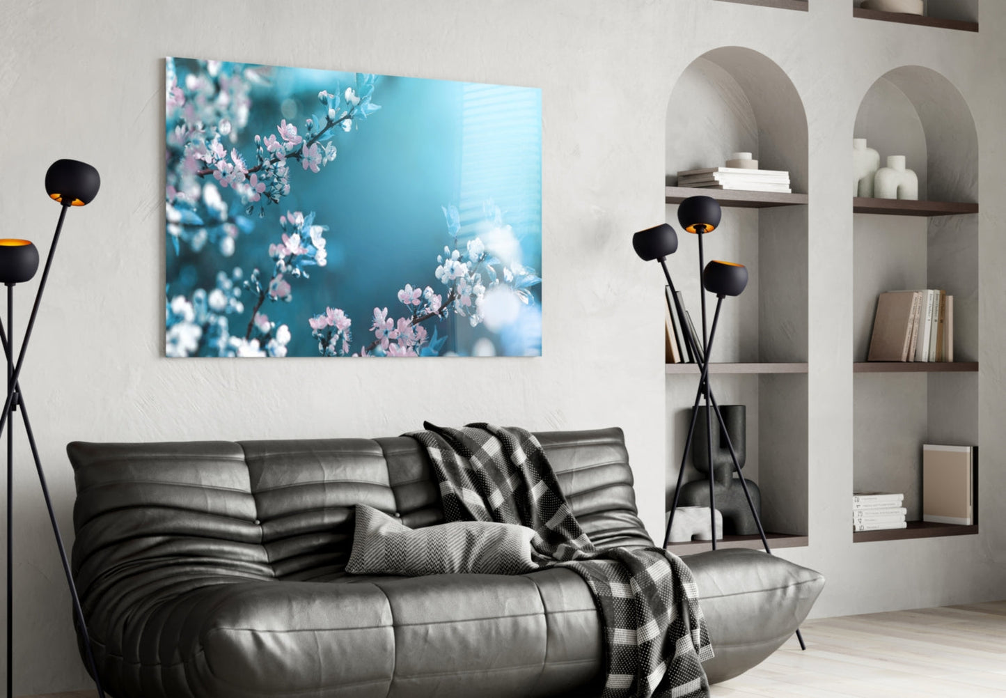 Glass wall art depicting pink and white spring blossoms against turquoise sky, displayed above black leather sofa in modern living room.