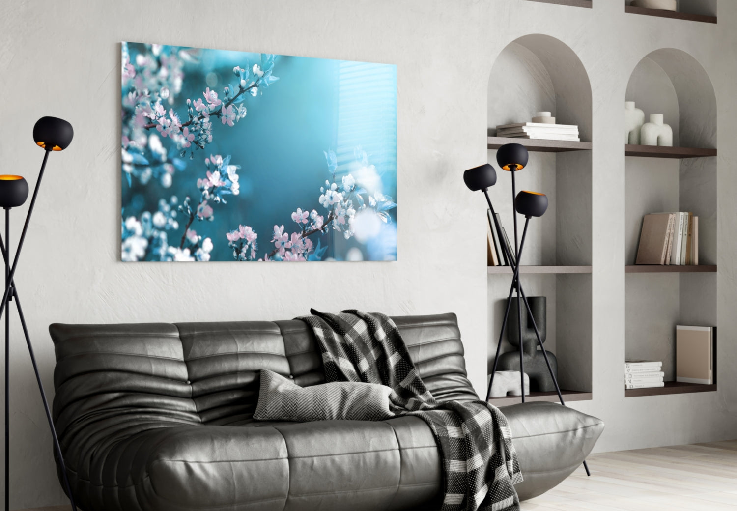 Glass wall art depicting pink and white spring blossoms against turquoise sky, displayed above black leather sofa in modern living room.