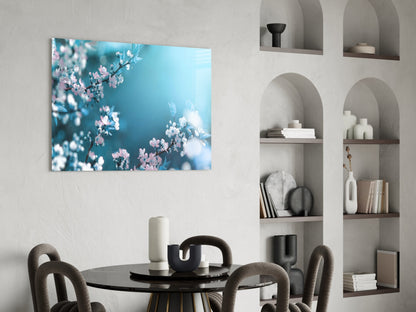 Glass wall art featuring pink and white spring blossoms against a turquoise blue sky, displayed above a black dining table.
