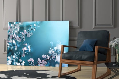 Glass wall art featuring pink blossoms on turquoise background displayed in modern living room with wooden chair.