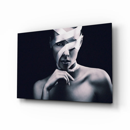 Black and white portrait of woman with white fabric wrapped around head, bare shoulders, dark background, mounted on glass panel.