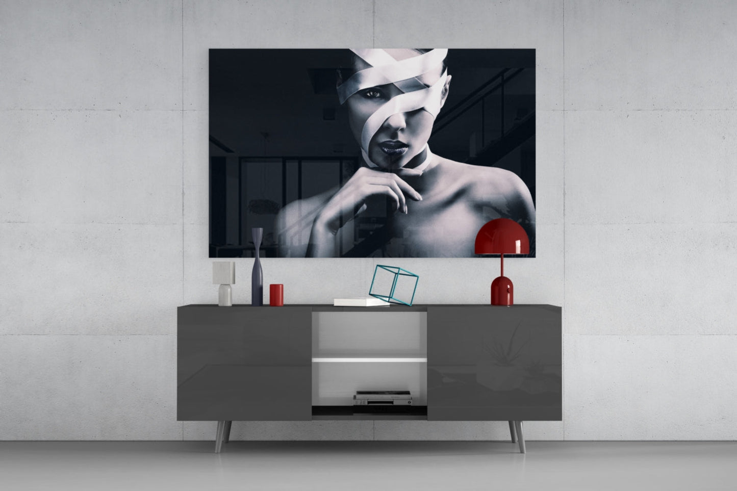 Modern living room with black and white portrait glass art mounted above gray media console with red accent lamp and decorative objects.