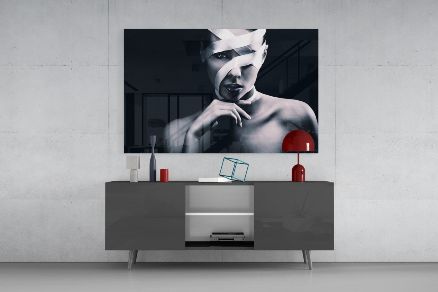 Modern living room with black and white portrait glass art mounted above gray media console with red accent lamp and decorative objects.