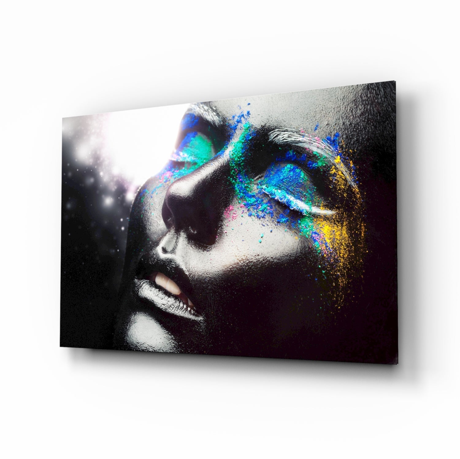 Profile view of female face in black and white with vibrant blue, cyan, yellow, and magenta powder dispersing across right side on glass panel.