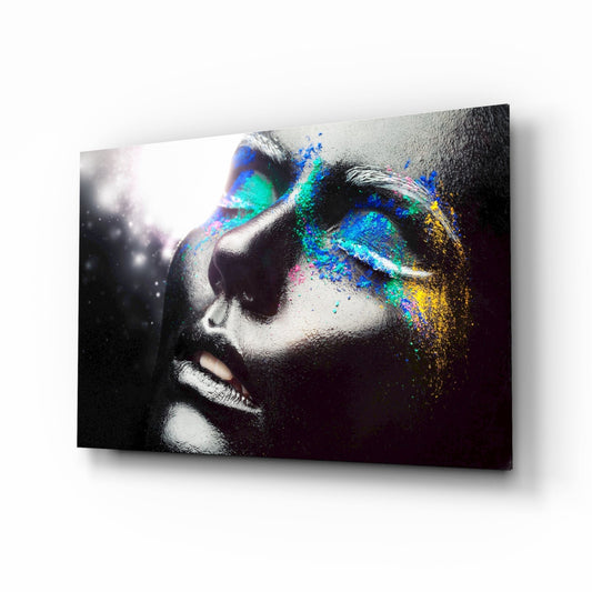 Profile view of female face in black and white with vibrant blue, cyan, yellow, and magenta powder dispersing across right side on glass panel.