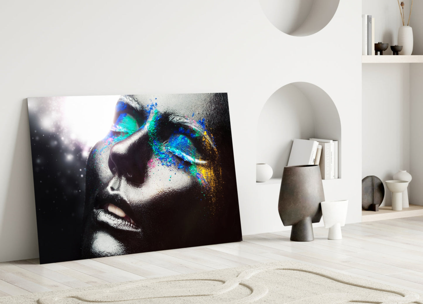 Colorful glass wall art leaning against white wall displays female portrait with vibrant blue, green, and yellow paint splatter effects on dark background.