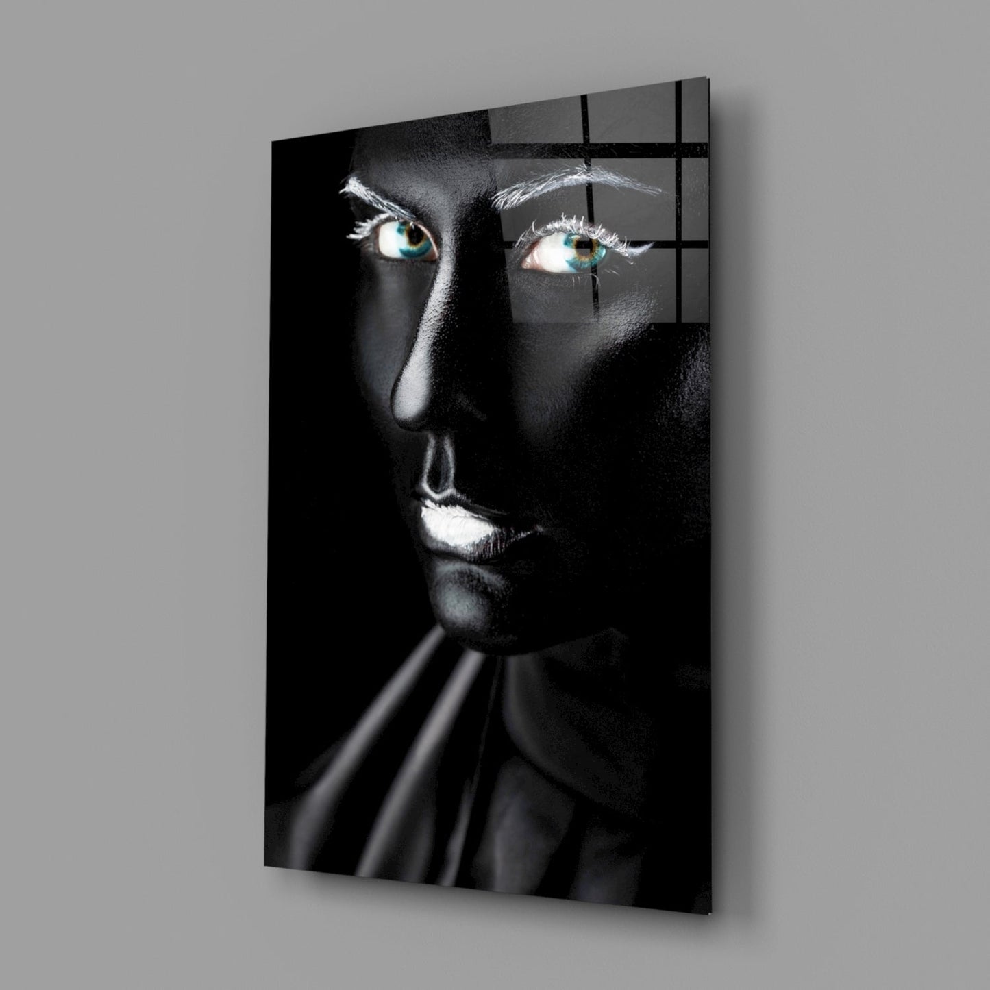Black and white glass portrait with striking turquoise eyes, illuminated face against dark background, mounted on gray wall.