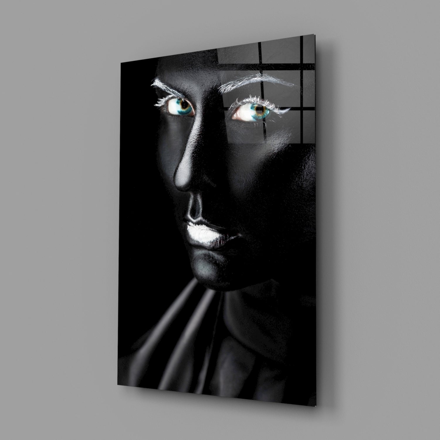 Black and white glass portrait with striking turquoise eyes, illuminated face against dark background, mounted on gray wall.