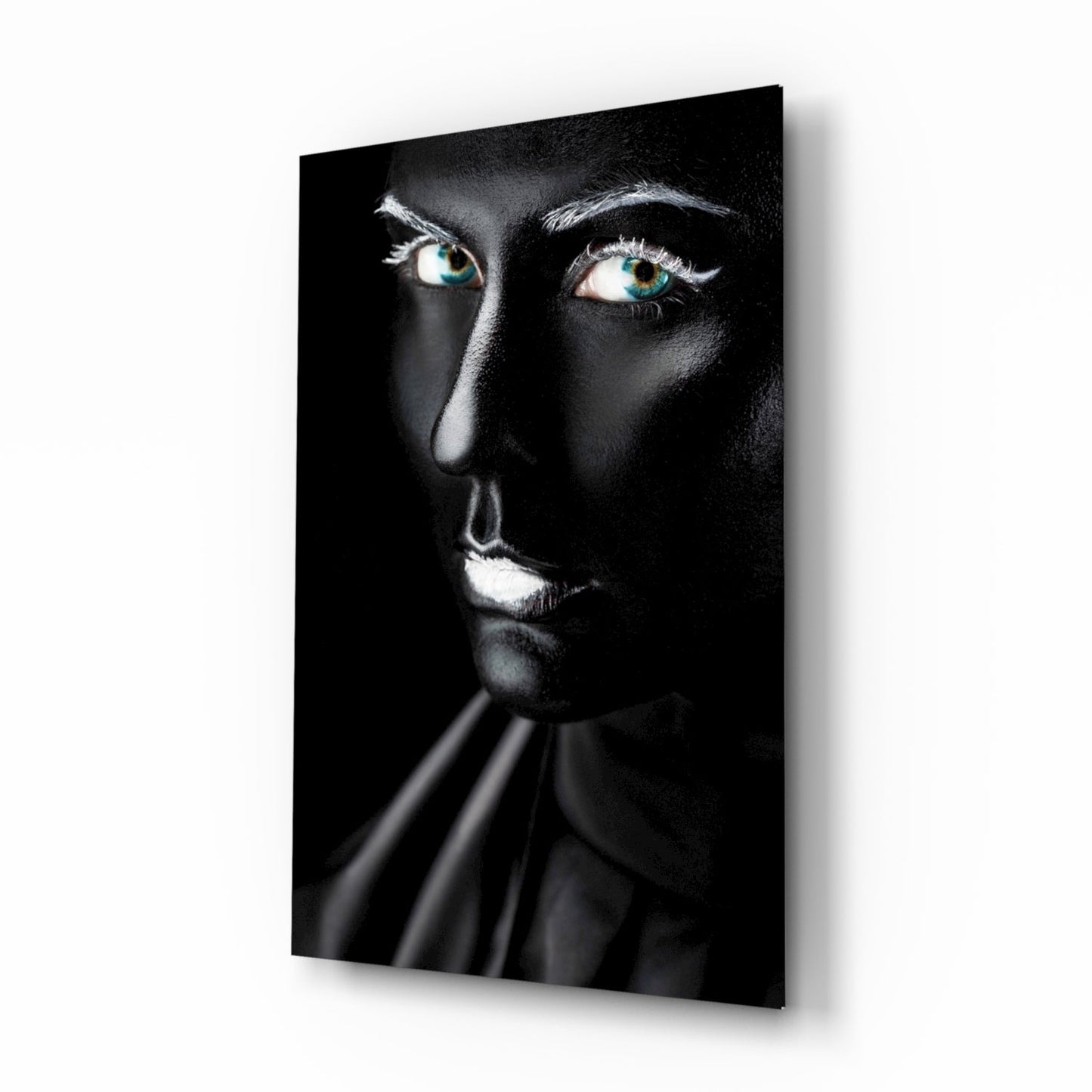 Woman's face with striking turquoise eyes against black background on glass wall art, displayed at angle.