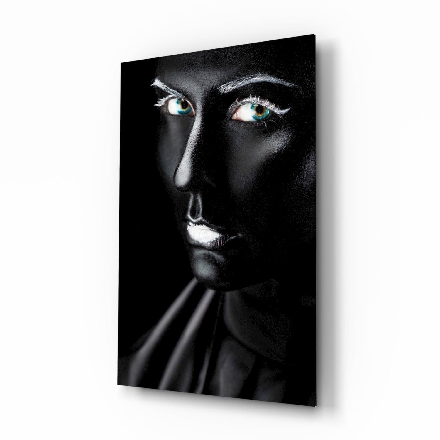 Woman's face with striking turquoise eyes against black background on glass wall art, displayed at angle.