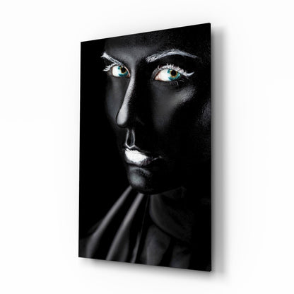Woman's face with striking turquoise eyes against black background on glass wall art, displayed at angle.