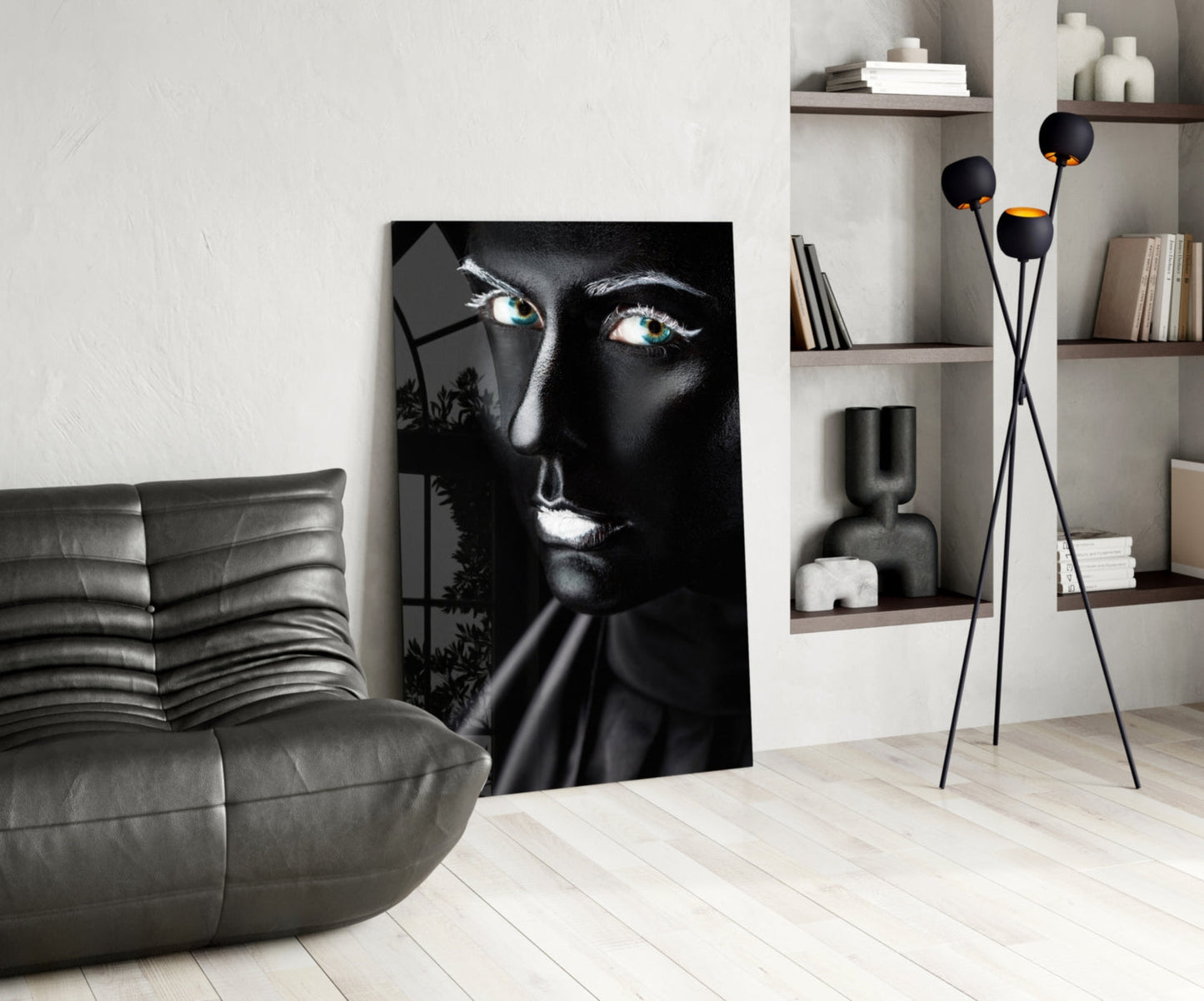 Modern living room with black and white glass portrait artwork leaning against white wall beside gray leather chair.