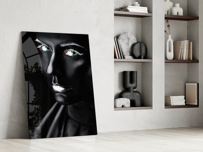 Black and white glass portrait with striking turquoise eyes leaning against white wall beside shelving unit.