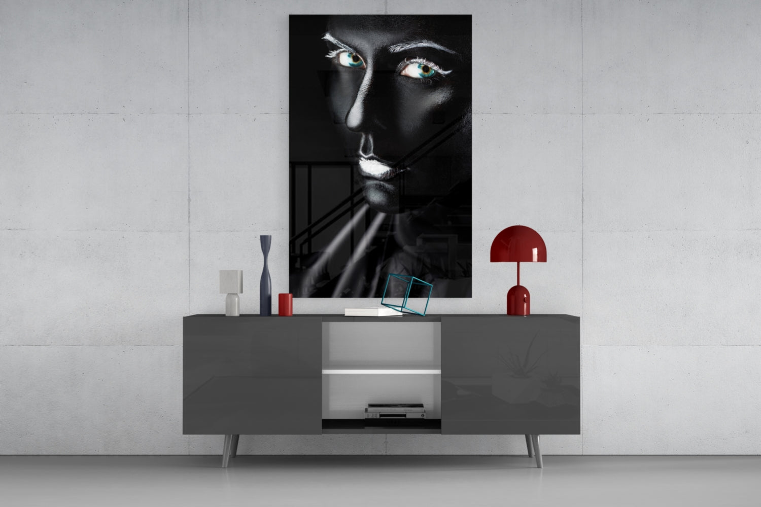 Black and white glass portrait with turquoise eyes displayed above gray media console with red accent lamp and decorative objects.