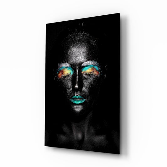 Glass wall art panel mounted at an angle showing a grayscale face with teal and gold eyeshadow and lips against black background.