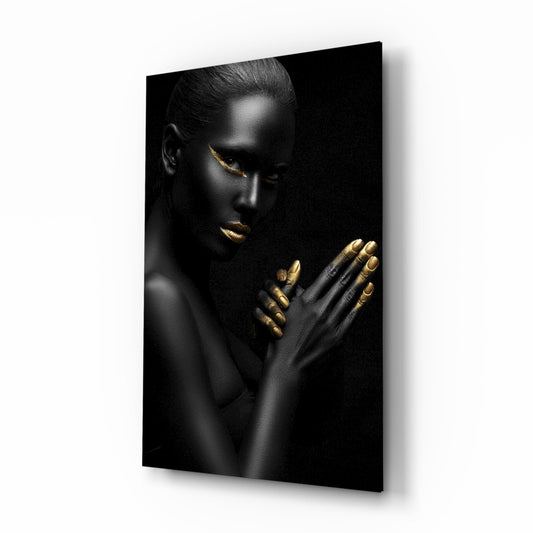 Black and gold portrait of a woman with praying hands and gold-accented lips on glass, angled view showing shadow on white background.