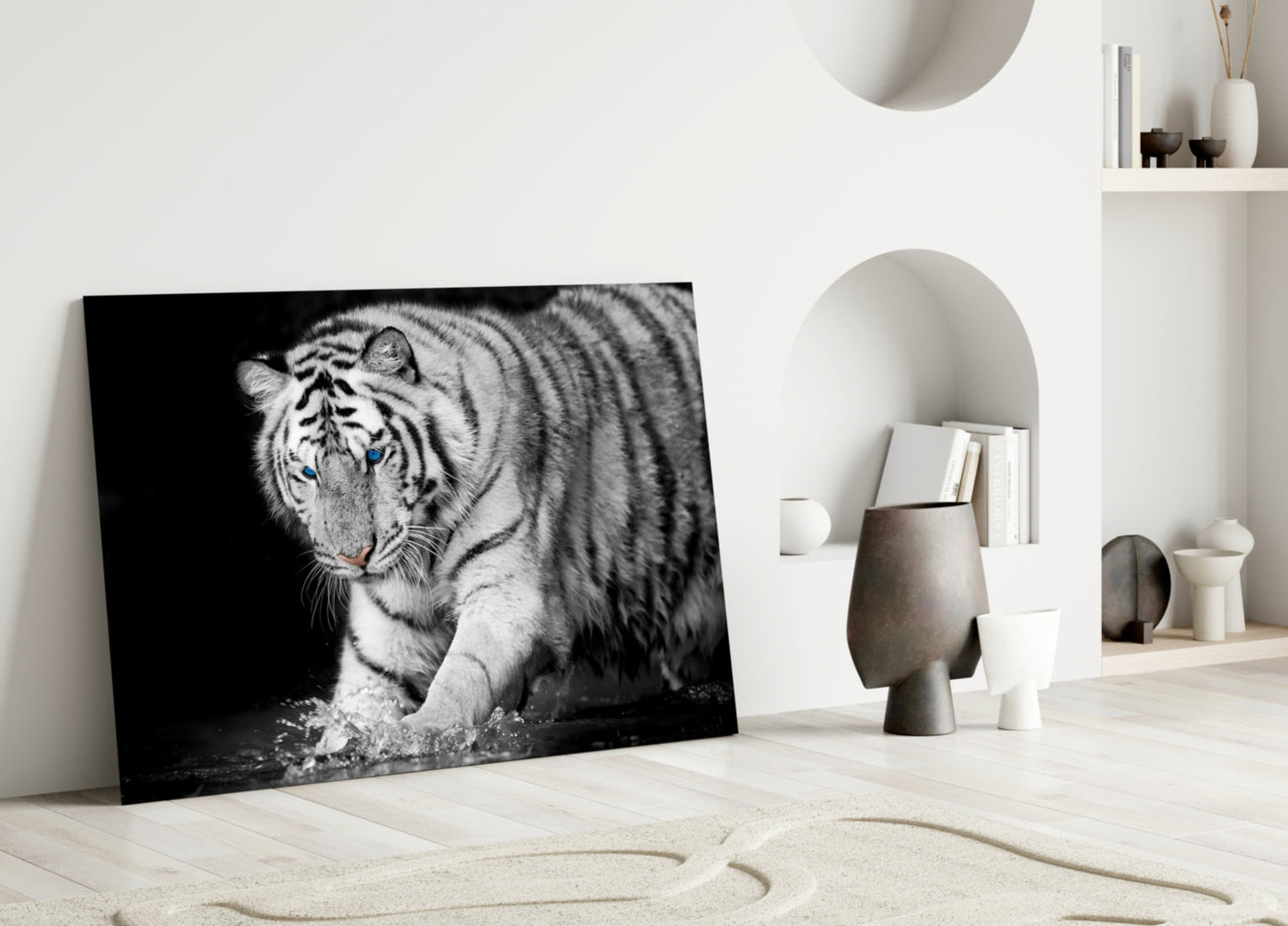 Black and white glass wall art depicting a tiger with blue eyes leaning against a white wall in a minimalist interior setting.