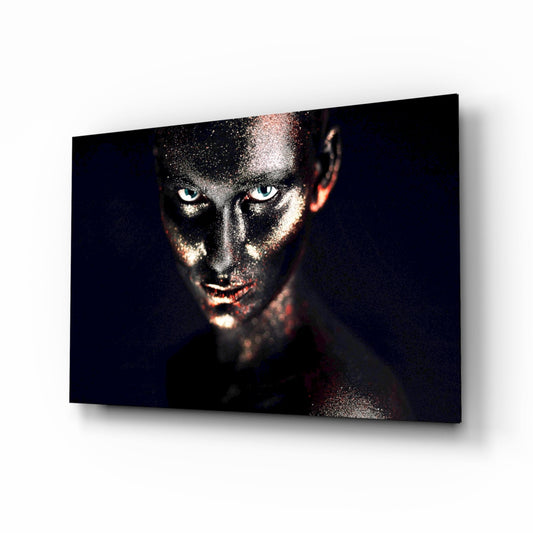 Glass wall art featuring a woman's face with glitter makeup, striking blue eyes, and dark background with copper accents, displayed at an angle.
