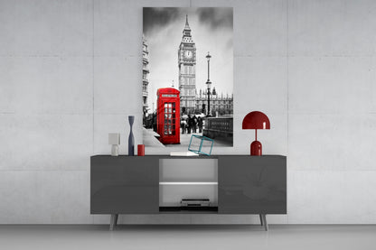 Black and white London street scene with iconic red telephone box and Big Ben displayed on glass wall art above gray console table with red decorative accessories.