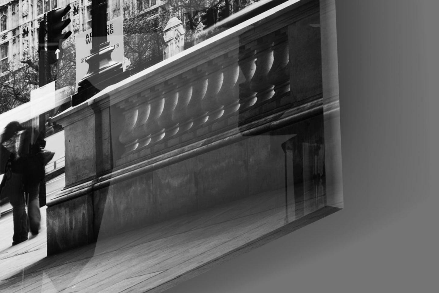 Black and white photograph showing glass wall art mounted on building facade with decorative molding and street-level storefront, angled perspective.