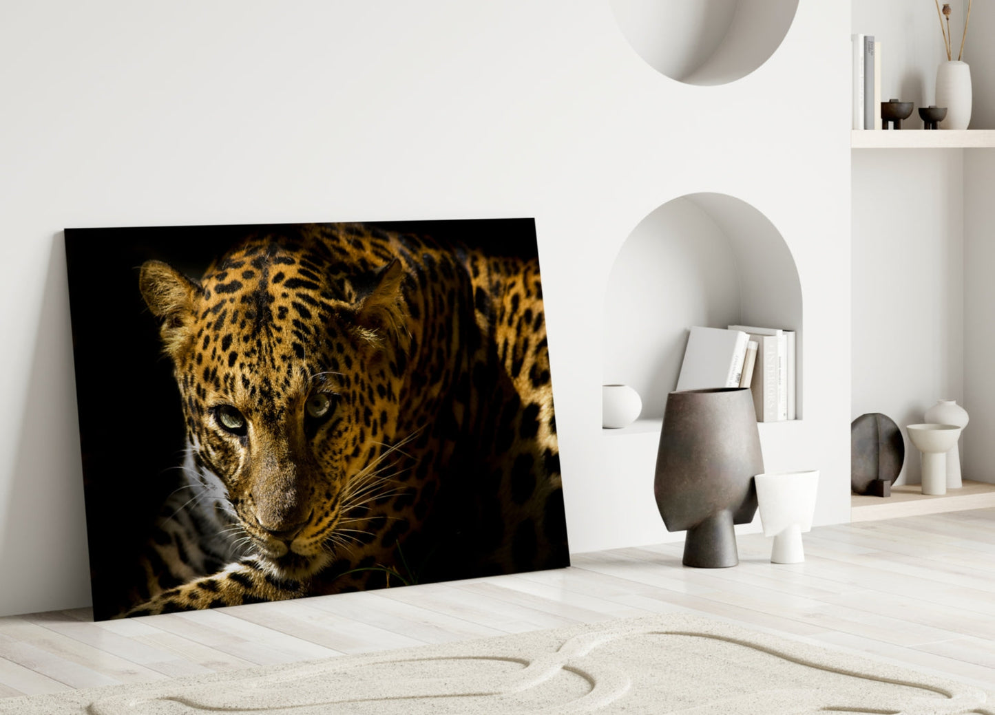 Leopard glass wall art leaning against white wall in minimalist interior, showing golden spotted big cat against black background.