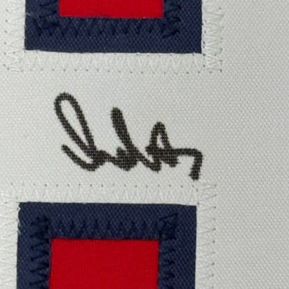 Close-up of handwritten signature in black ink on white fabric with navy and red striped borders.