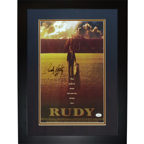 Framed movie poster for "Rudy" showing a man standing in a football field with stormy sky, featuring gold borders and an autographed signature in the upper left corner.