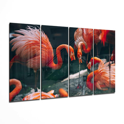 Four-panel glass wall art displaying vibrant orange and red flamingos with curved necks against dark background, shown at angled perspective.