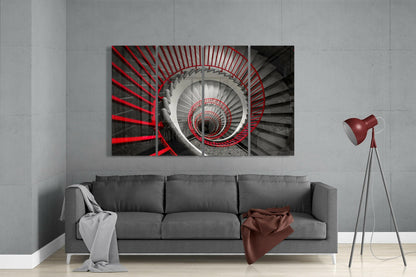 Four-panel glass wall art depicting a spiral staircase with red railings receding into darkness, displayed above a gray sofa in a modern living room.