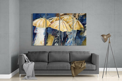 Four-panel glass wall art depicting figures with yellow umbrellas against a deep blue background, displayed above a gray sofa in a modern living room.