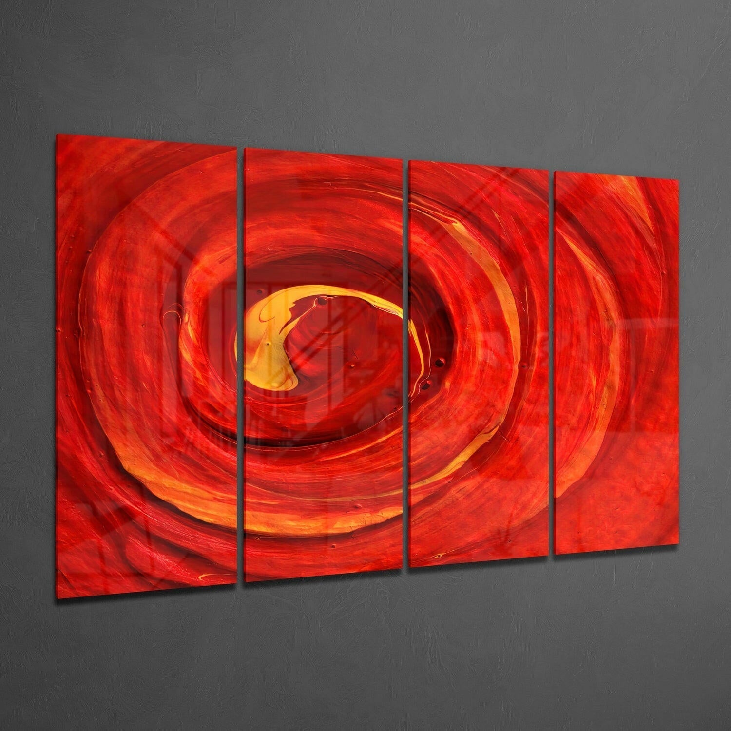 Four-panel red glass wall art displaying a swirling vortex with yellow and orange center, mounted on gray wall at angle.