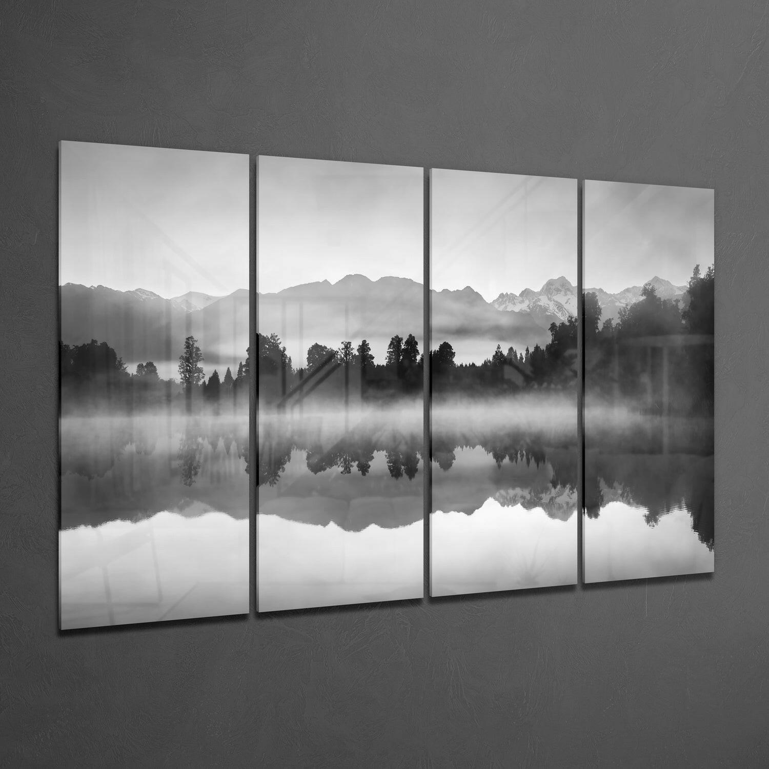 Four black-framed glass panels displaying a misty mountain landscape with forested shoreline reflected in still water, mounted on gray wall.