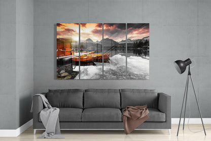 Four-panel glass wall art depicting orange boats on a misty lake with mountains and sunset sky, displayed above a gray sofa in a modern living room.
