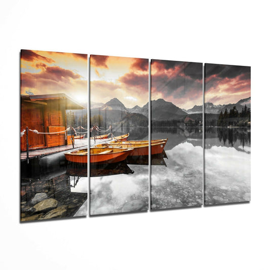 Four-panel glass wall art showing orange boats moored at a wooden dock beside an alpine lake at sunset, with mountains and forest in the background.