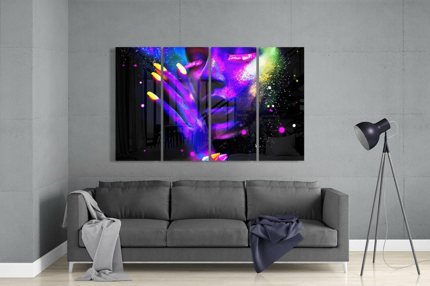 Four-panel neon abstract glass wall art displaying vibrant purple, magenta, yellow, and blue glowing particles and light streaks on black background, installed above gray sofa in modern living room.