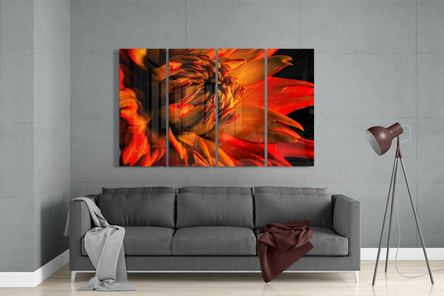 Four-panel glass wall art displaying vibrant red and orange gerbera daisy petals, installed above a gray sofa in a modern living room setting.