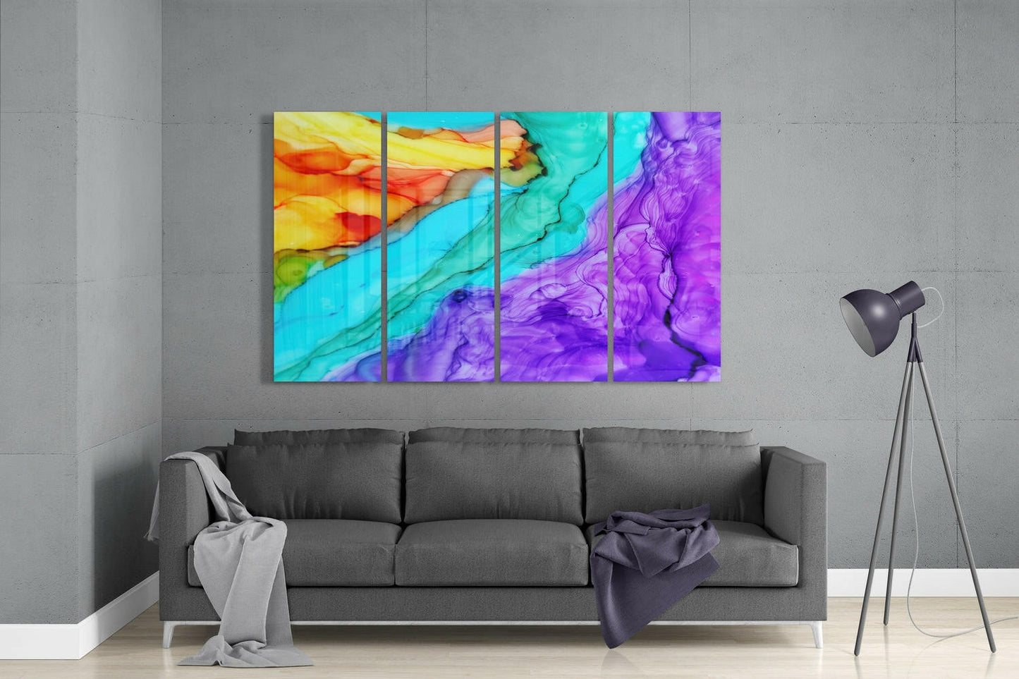 Four-panel glass wall art displaying flowing abstract watercolor in yellow, orange, cyan, blue, and purple tones hanging above gray sofa in modern interior.