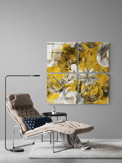 Four-panel glass wall art with yellow, white, and brown botanical flowers displayed above a beige lounge chair in a minimalist interior setting.