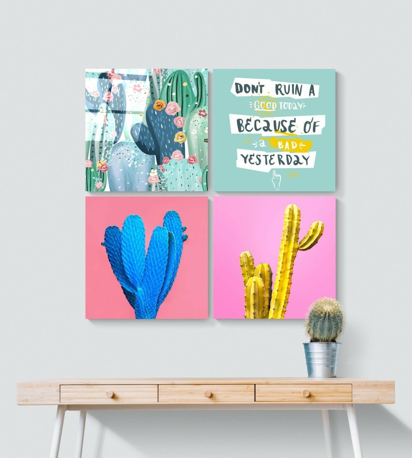 Four colorful glass cactus wall art panels displayed on wooden desk with potted cactus, featuring turquoise florals, motivational text, and pink and yellow cacti designs.