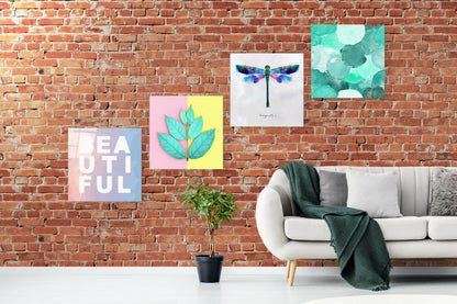 Room setting displaying four glass wall art panels on exposed brick: pink "Beautiful" text, split pink-yellow panel with turquoise leaves, watercolor dragonfly, and turquoise bubble pattern.