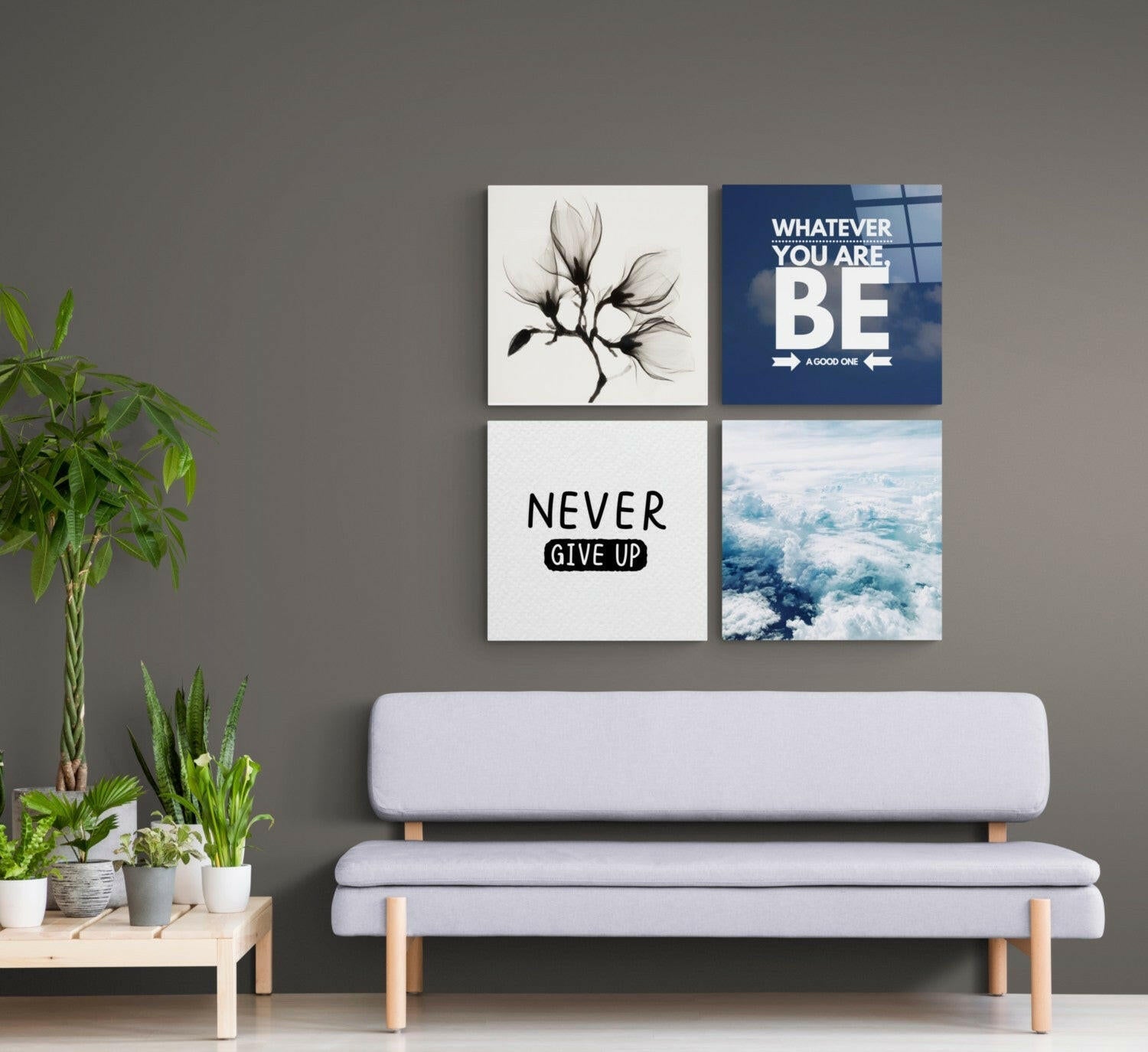 Four glass wall art panels arranged in a grid above a light gray bench, featuring a black flower sketch, blue motivational text, "Never Give Up" text, and an aerial cloud photograph.