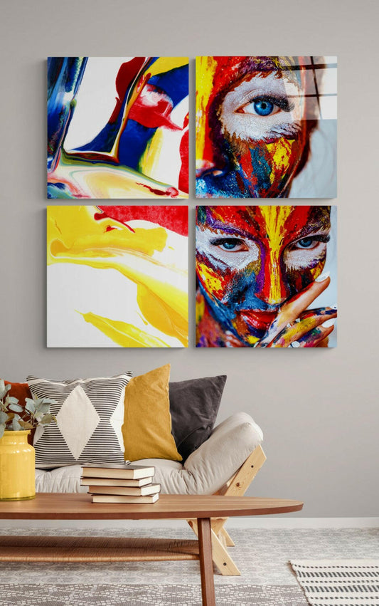 Four colorful glass panels featuring painted face designs in red, yellow, and blue mounted on a gray wall above a wooden bench with pillows and books.