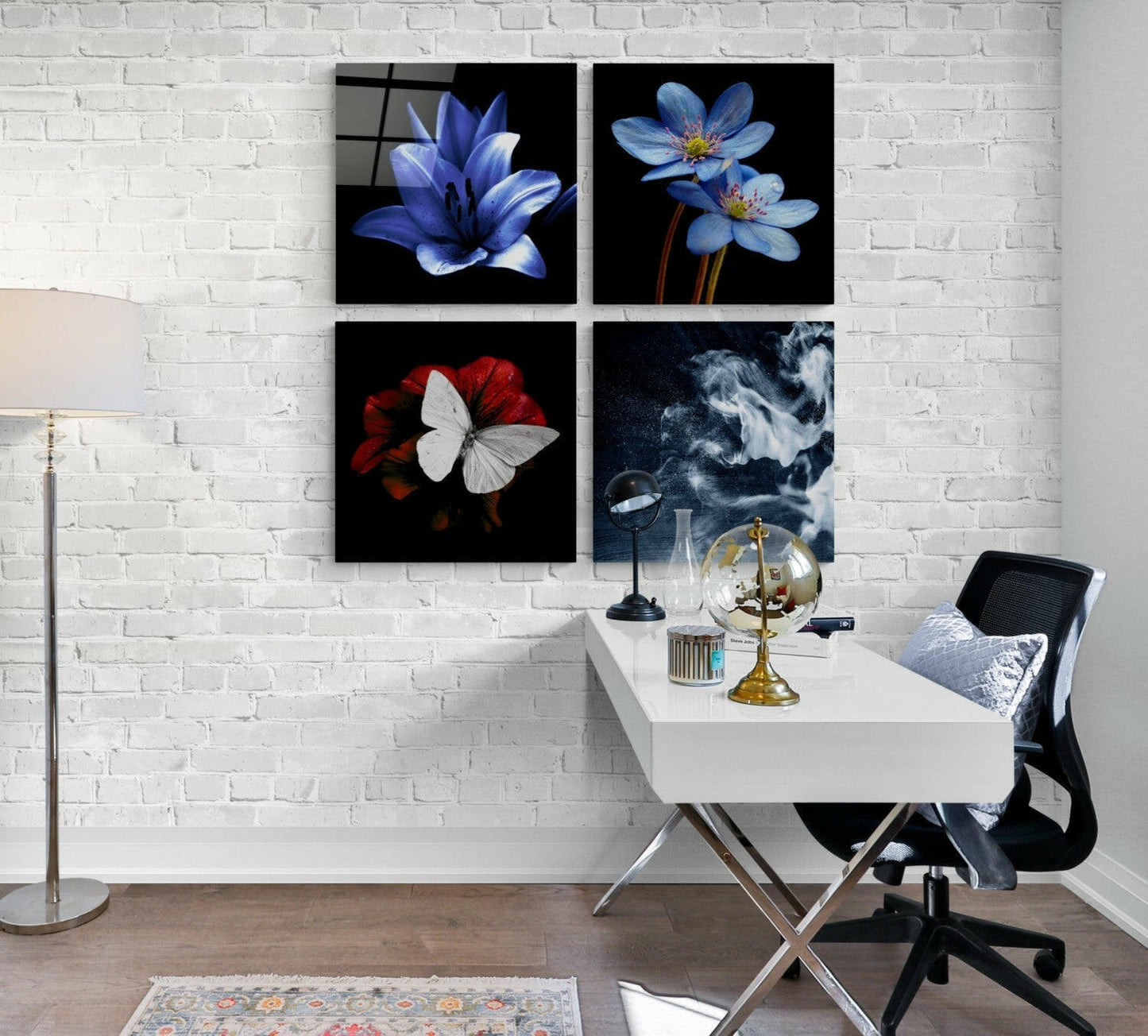 Four glass wall art panels displaying blue flowers, red flower with white butterfly, and abstract dark imagery mounted above white desk in modern office setting.