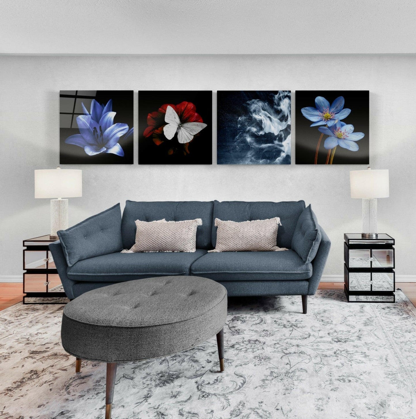 Four glass wall art panels featuring blue flowers, red and white butterfly, and stormy clouds displayed above a blue sofa in a living room setting.