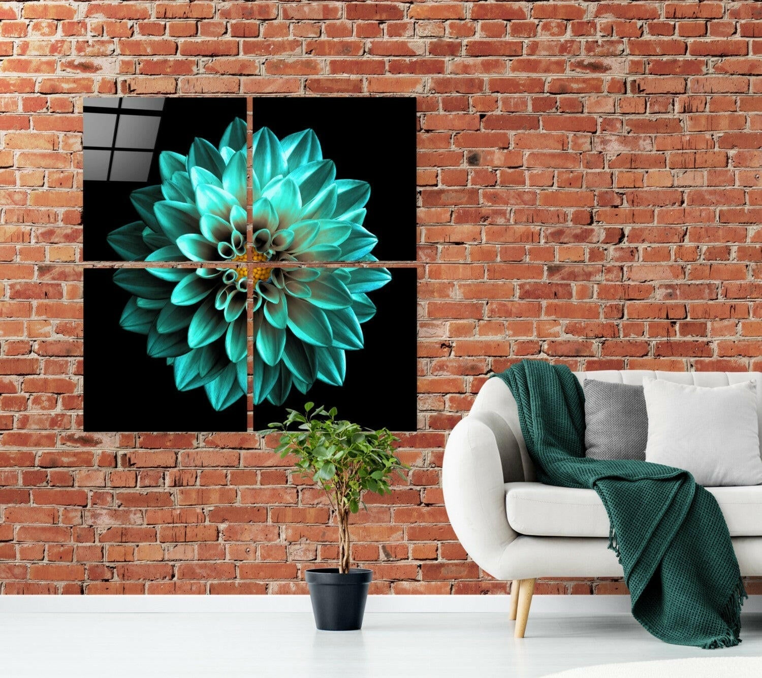 Four-panel glass wall art displaying a turquoise dahlia flower on black background, installed above white sofa with green throw blanket in brick loft interior.