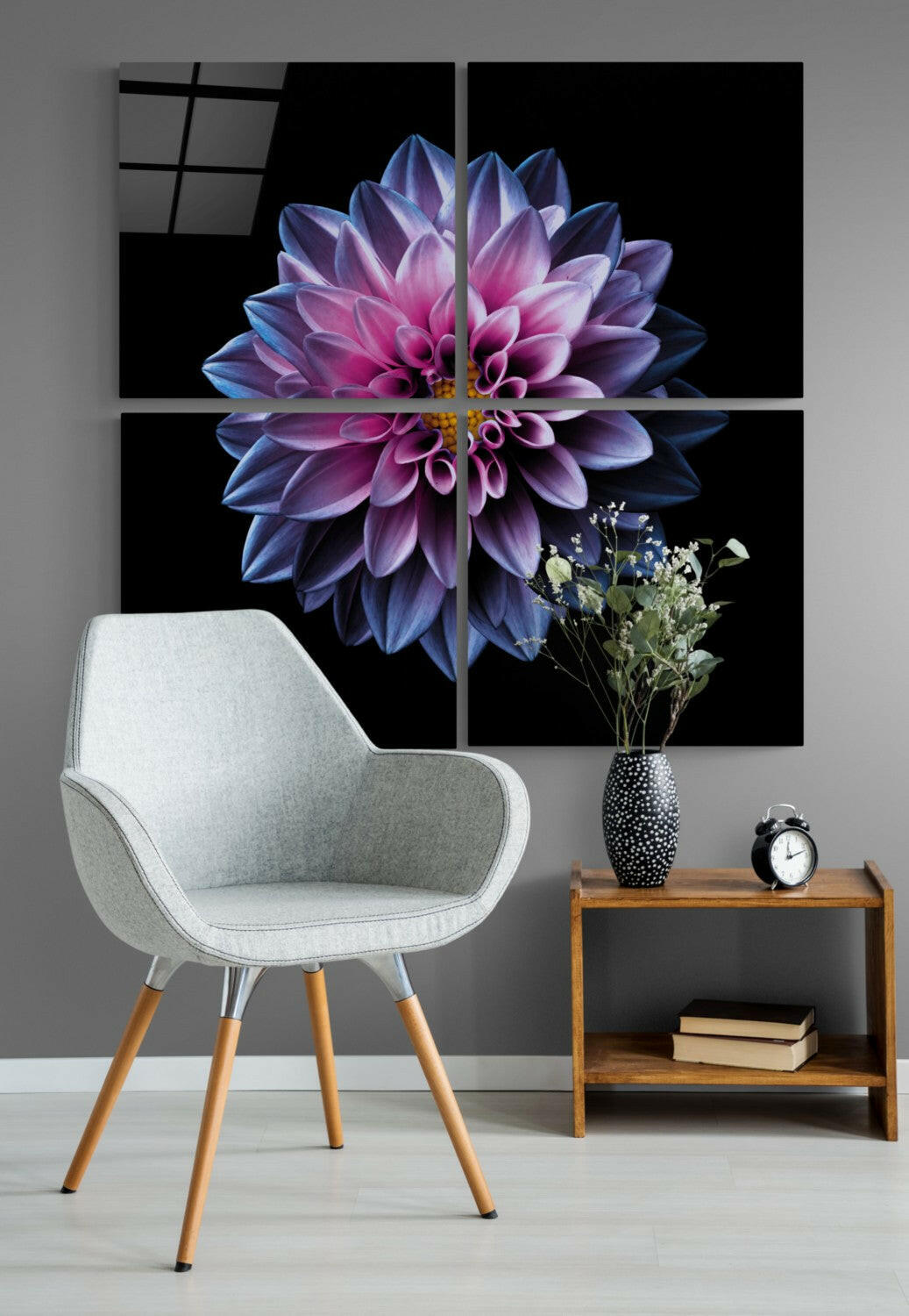 Four-panel glass wall art displaying a purple and pink dahlia flower on black background, installed above a gray chair and wooden side table with décor.