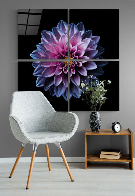 Four-panel glass wall art displaying a purple and pink dahlia flower on black background, installed above a gray chair and wooden side table with décor.