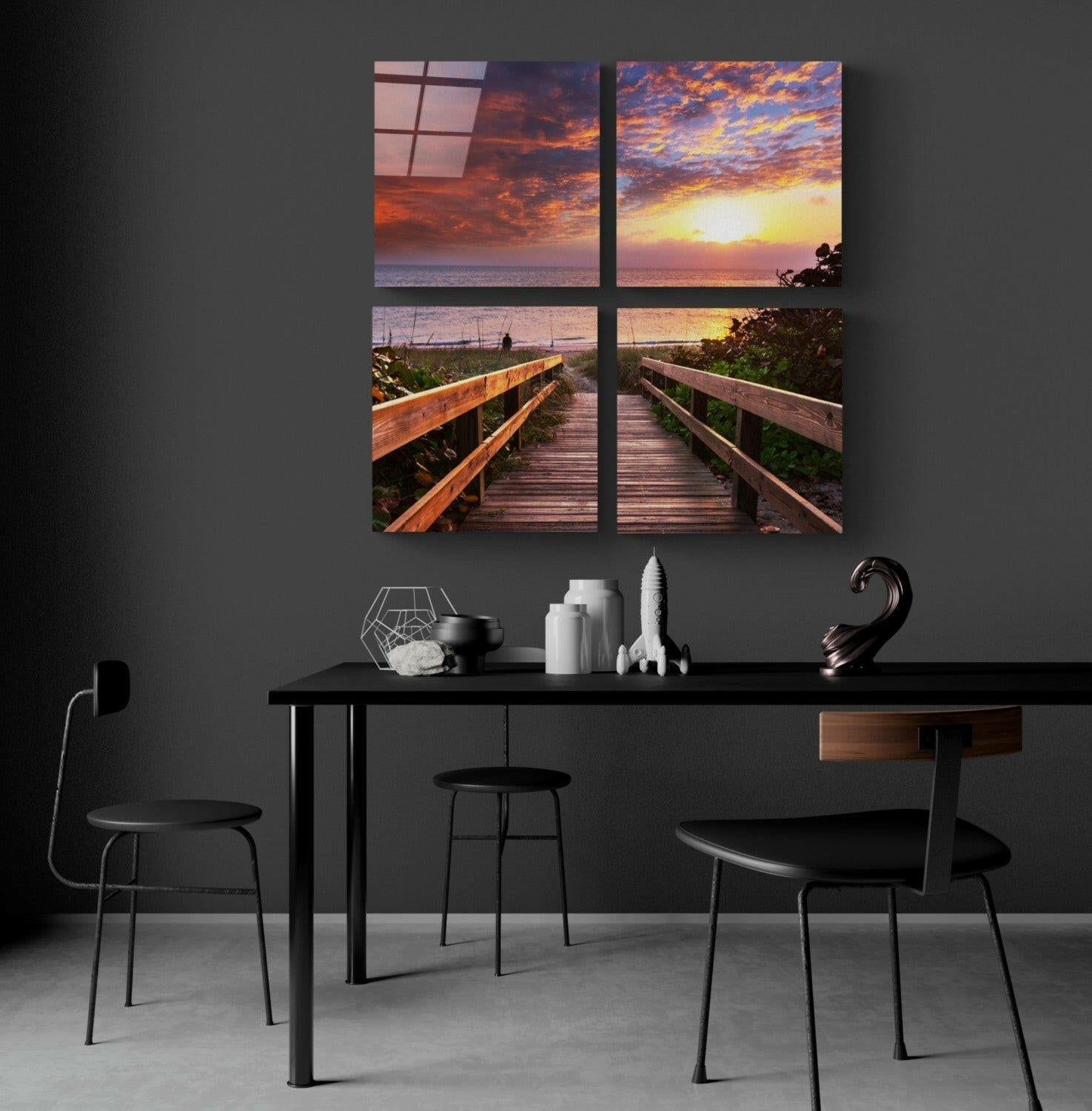 Four-panel glass wall art depicting wooden boardwalk leading to sunset over ocean, displayed above black desk in modern interior.