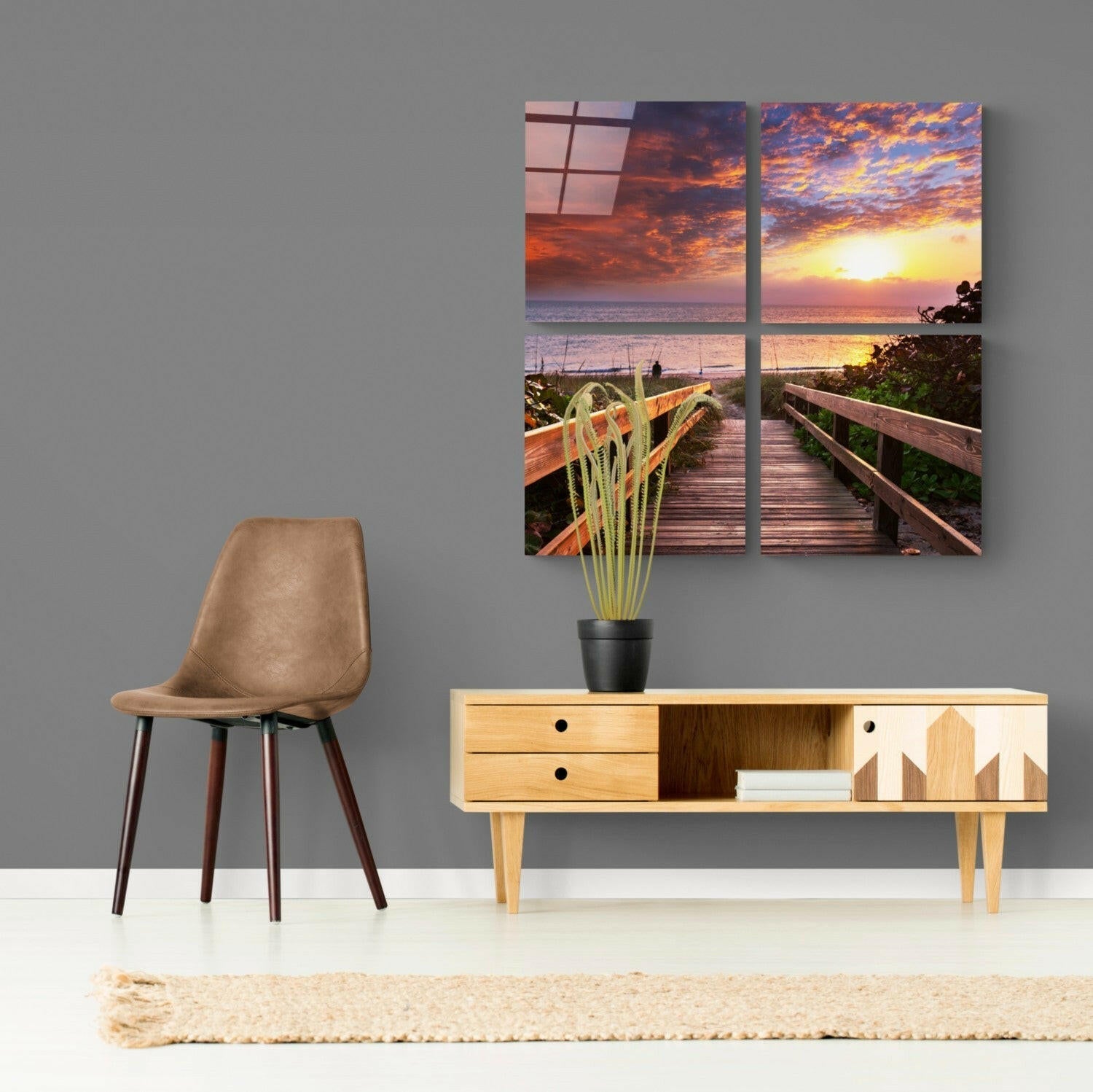 Four-panel glass wall art displaying a wooden boardwalk leading to a vibrant sunset over the ocean, installed above a mid-century modern console table with a potted plant.